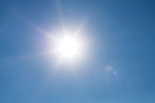 Bright sun shining radiantly in a clear blue sky, casting lens flares and illuminating the surroundings with a warm glow on a sunny day.